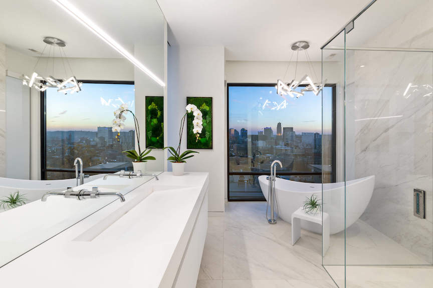 PureEdge Lighting Cirrus linear LED light above a long white vanity and mirror in a modern bathroom with a freestanding tub and city view