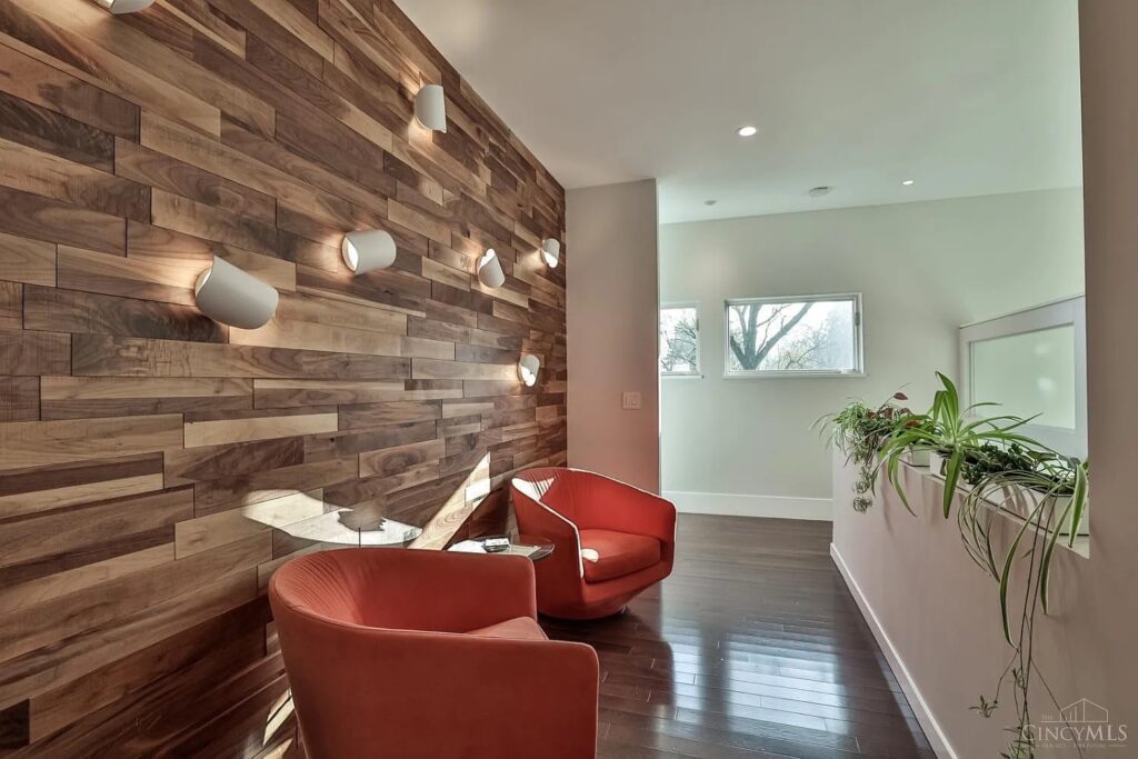 Row of white FontanaArte Io LED wall sconces washing light up and down a reclaimed wood accent wall in a modern living room with red lounge chairs