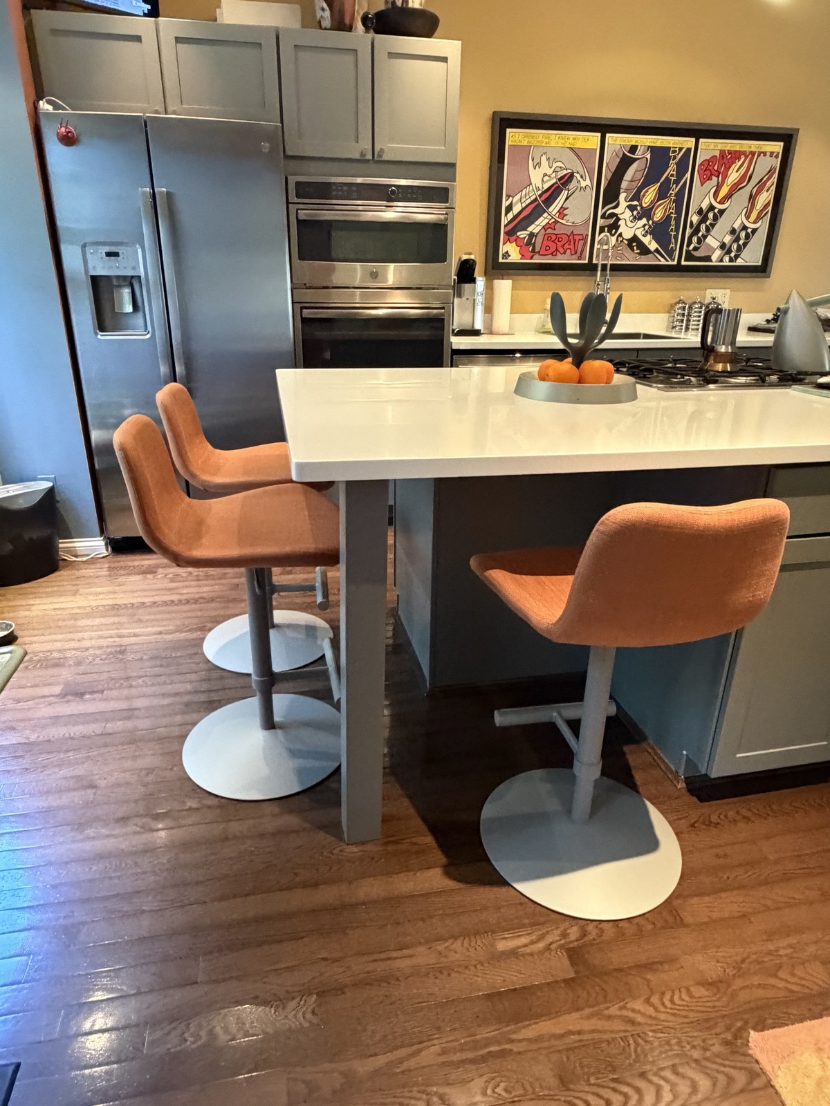Three orange Midj Dalia swivel stools beside a stainless steel appliance wall