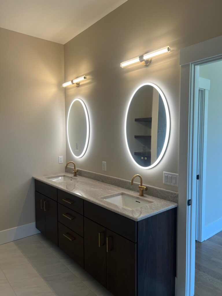 Round Eurofase LED lighted mirrors with a slim vanity light above, over a dark double vanity