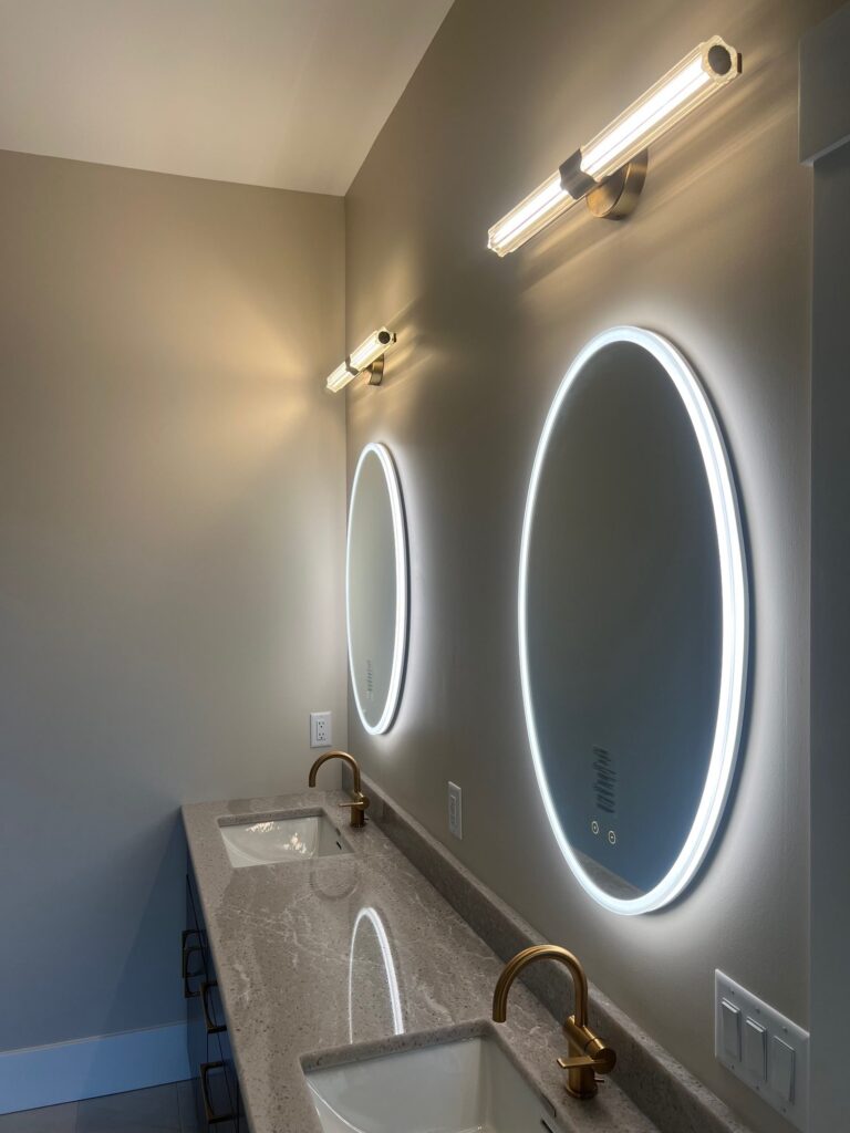 Eurofase round LED lighted mirror with a halo of light and a vanity light above a dark vanity