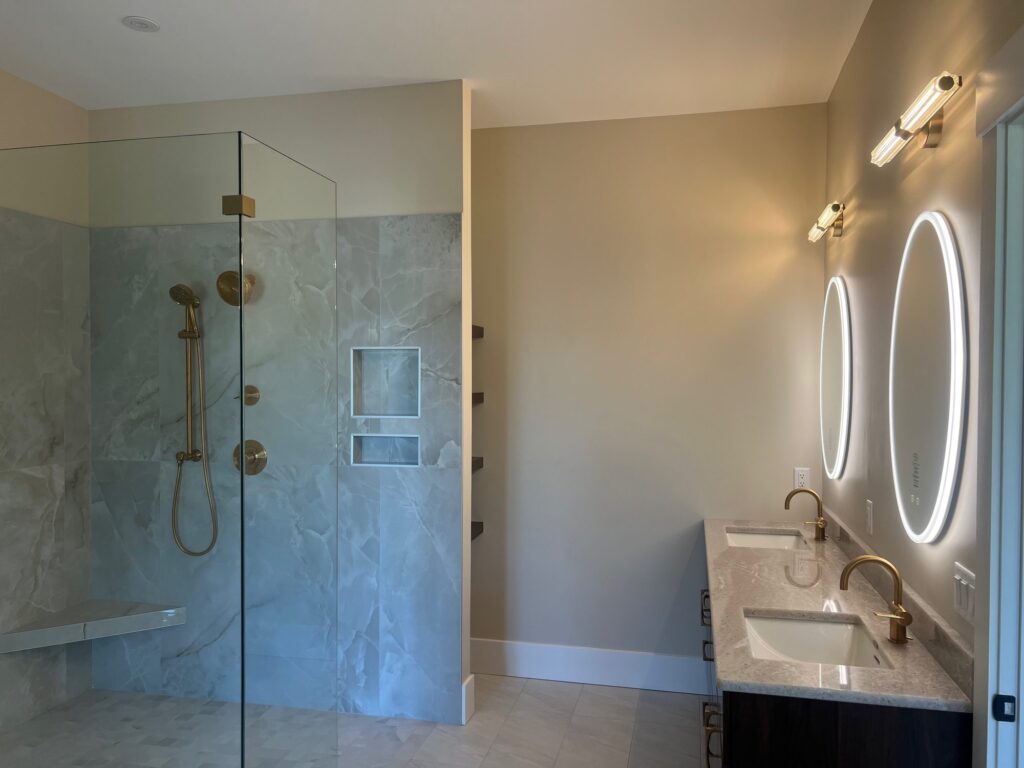 Bathroom with a glass shower and a round Eurofase LED lighted mirror and vanity light over the sink