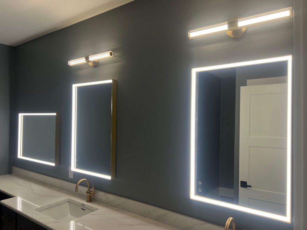 Two rectangular Eurofase LED lighted mirrors with glowing edges and linear vanity lights above, on a dark grey wall