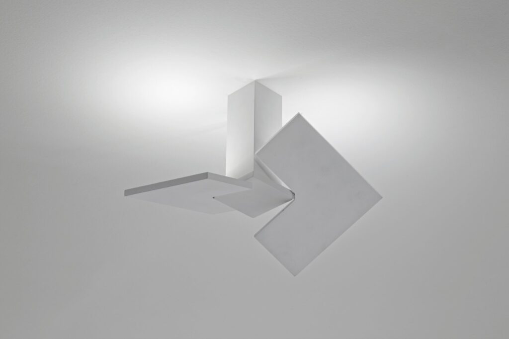 Lodes Puzzle Twist wall light: white square plates turned at angles, throwing geometric light across a grey wall