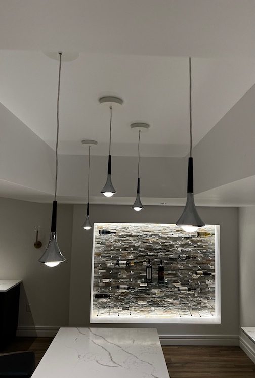 Rain pendants over a basement bar with a lit stone wall