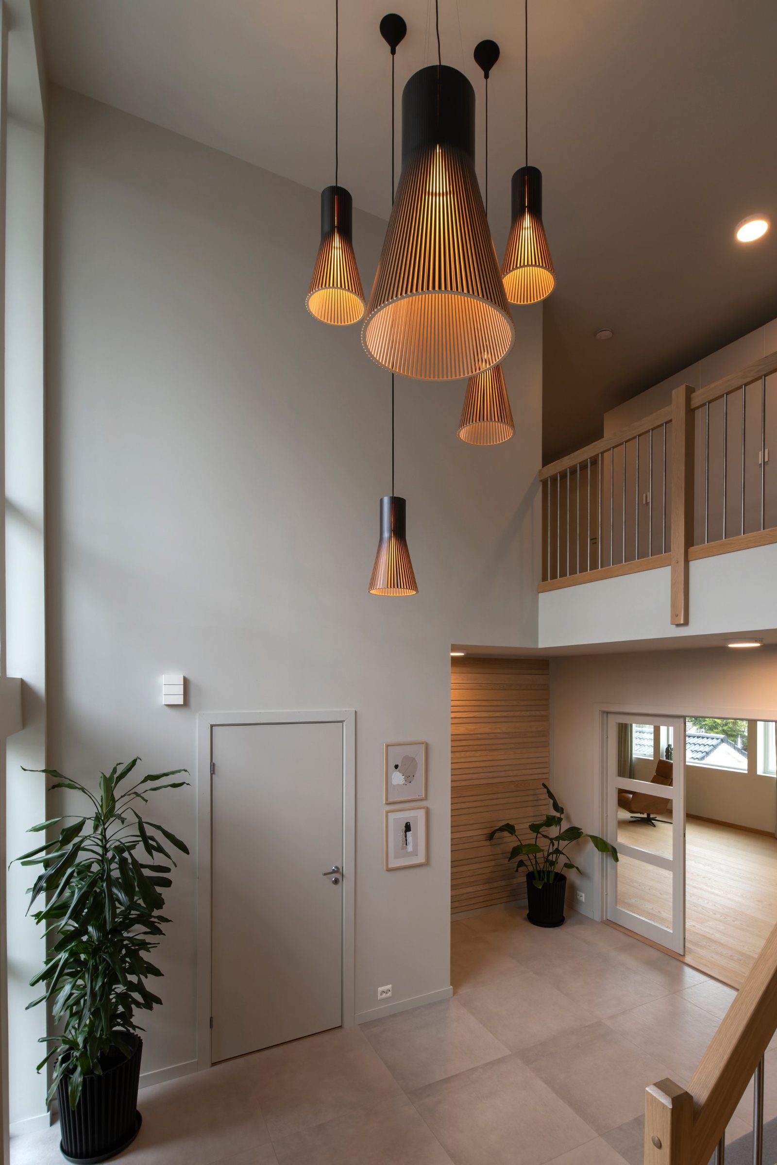 Cluster of black-topped Secto wooden pendants in varied sizes hanging in a double-height foyer with a gallery landing