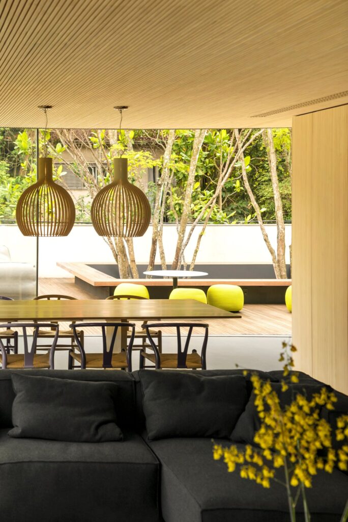 Two Octo 4240 wooden pendants over a dining table with a garden courtyard beyond, FIO House, São Paulo