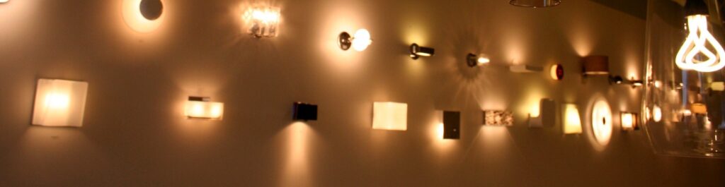 A long showroom wall lined with modern wall sconces casting pools of warm light, at Switch Lighting & Design in Cincinnati